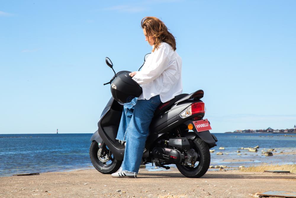 Kvinna fixar mopedhjälmen sittandes på en moped Viarelli GT1